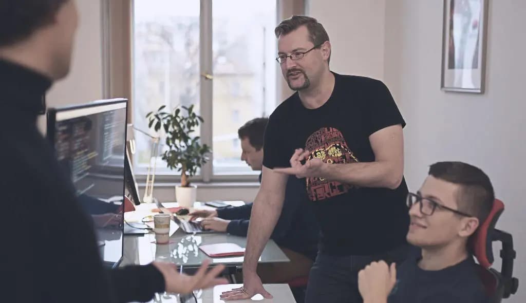 Three Salsita engineers in discussion around a monitor – one standing and explaining, one smiling, one working at the screen