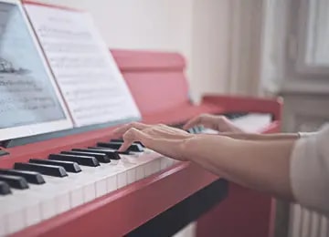Person playing a red digital piano with sheet music on a stand in the Salsita office
