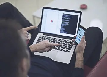 Developer working on a laptop with code on screen and a smartphone nearby