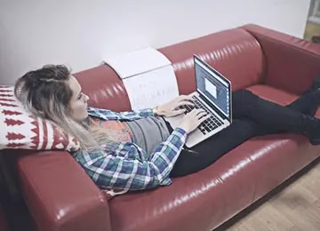 A Salsita employee lying on a red leather couch working on a laptop