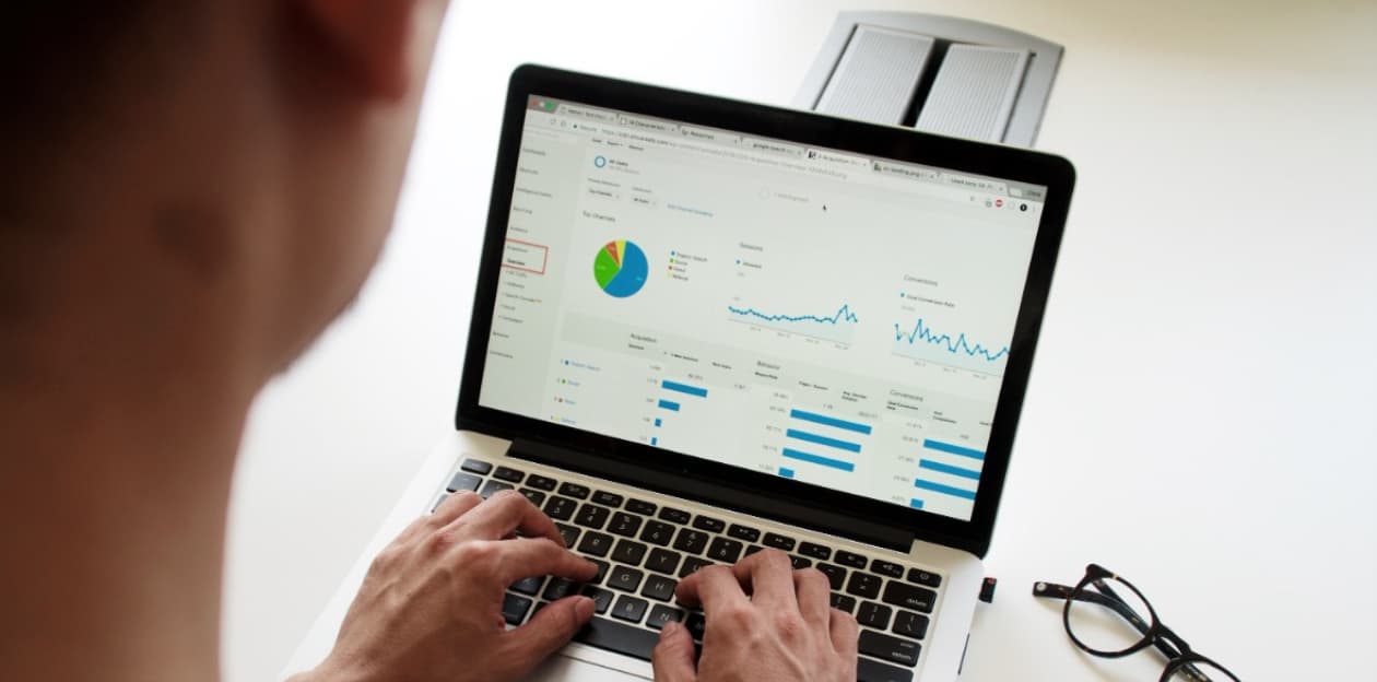 Person viewing analytics on a laptop screen with graphs and charts, including a pie chart and line graphs