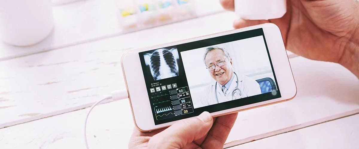 A person holds a smartphone showing a video call with a smiling doctor and medical data including an X-ray of lungs